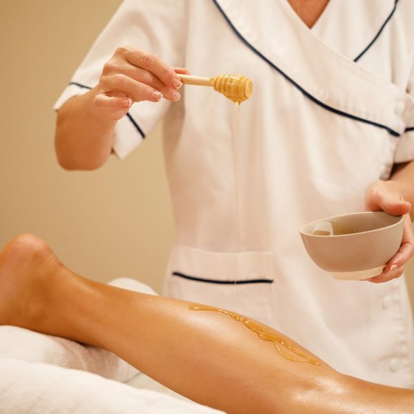 unrecognizable-therapist-pouring-honey-while-massaging-woman-s-leg-spa-salon